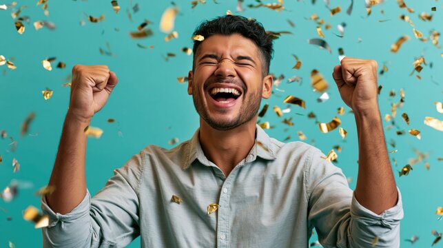 Young man celebrating with both fists raised laughing amidst falling gold confetti