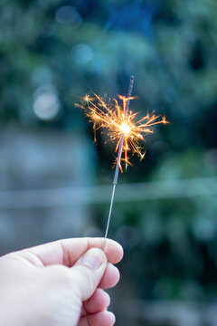 Hand holding glowing burning sparkler firework creates joyful light and bright spark during evening outdoor party celebration, bringing happy feeling and magical festive mood