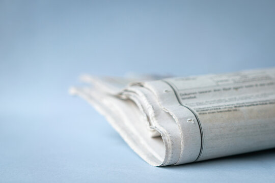 Newspaper folded on top of desk, isolated on light blue background. Copy space.