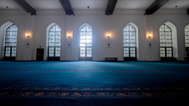 Interior of a prayer hall in a large mosque with blue carpet and arched interior architecture building religious spiritual peaceful community structure lighting daylight gathering heritage