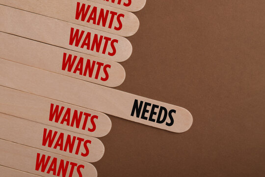 Wooden sticks labeled needs and wants illustrate consumer priorities, purchasing decisions, budgeting, financial planning, and the difference between essentials and desires.