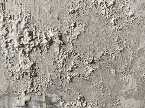 A close-up view of a damaged wall with peeling paint and rough, textured surface, showing signs of wear and decay.