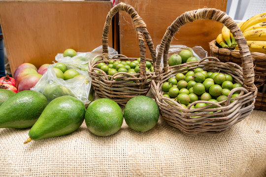 Fresh mamoncillo and ripe avocado showcasing healthy eating and tropical fruit variety in wicker baskets at a vibrant produce market stall