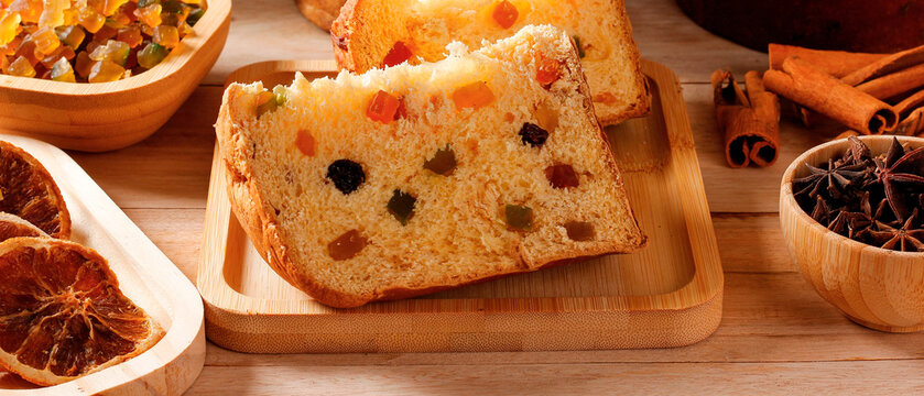 Classic slice Christmas panettone with candied fruit and spices on rustic wooden table.