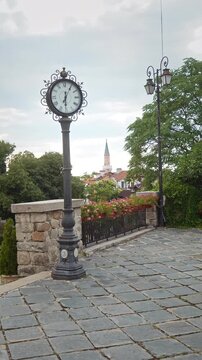 Vertical view of a decorated antique double-faced post clock with an Ottoman mosque minaret visible in the background in Plovdiv.