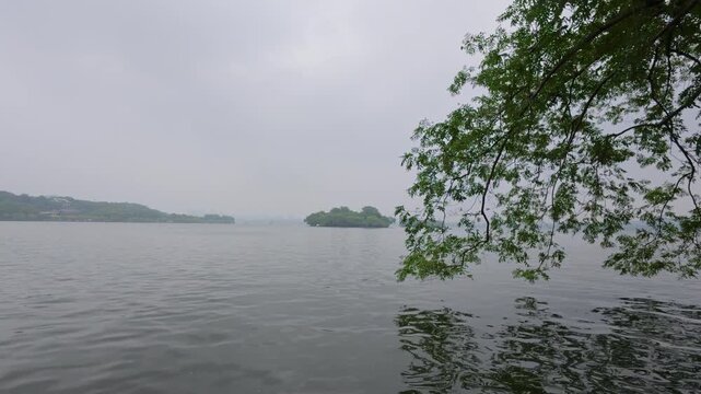 Overhanging tree branches framing misty West Lake, Hangzhou, China, with a distant island and reflections