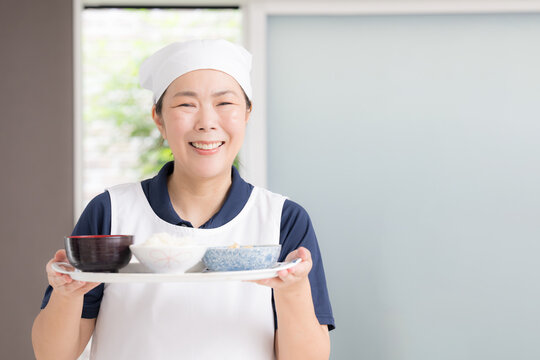 A smiling female staff member wearing a triangular headscarf as she prepares a meal at an elderly person&rsquo;s home; images of housekeeping services, meal preparation services, in-home care