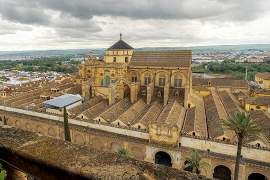 Mosque-Cathedral of Cordoba tiled roofs and cathedral dome seen over a mossy stone parapet with palm trees