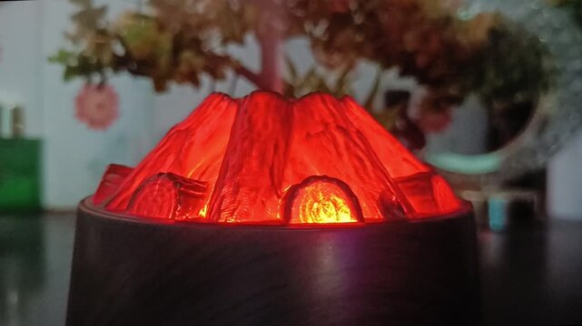 Close view of glowing red volcano diffuser with faux tree decor in background