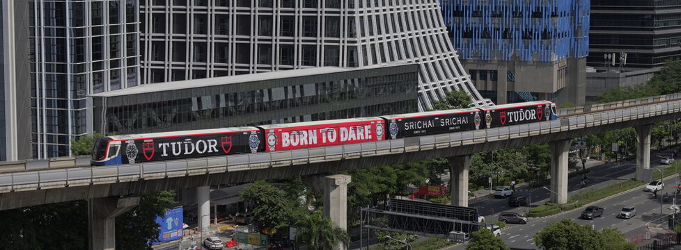 BTS Skytrain on an elevated track displays a full-wrap advertisement against a backdrop of modern high-rise buildings in Thai capital Bangkok