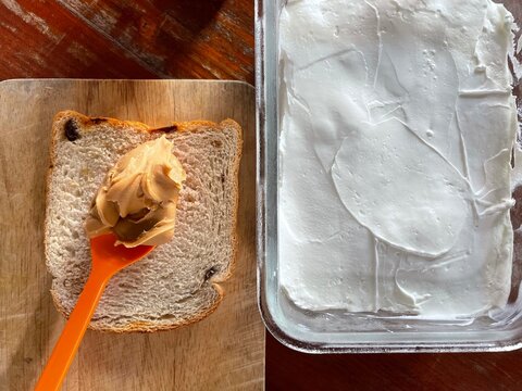Healthy breakfast preparation featuring creamy peanut butter on sliced whole wheat raisin bread, paired with a fresh tub of thick Greek yogurt. A nutritious, high-protein snack option. 