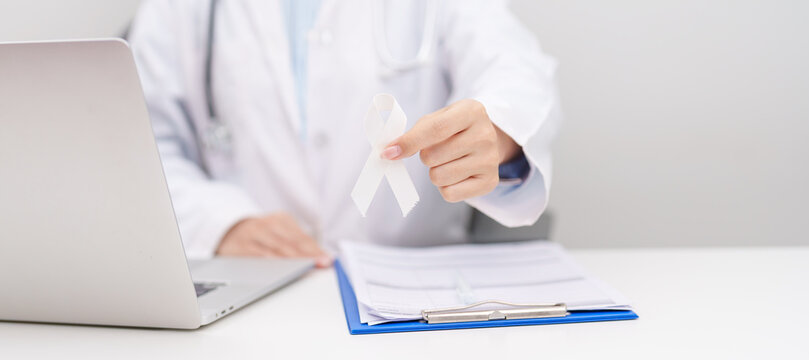 Doctor wearing lab coat giving white ribbon to patient for November Lung Cancer Awareness month, World Cancer Day, Healthcare consultation and empathy concept in hospital