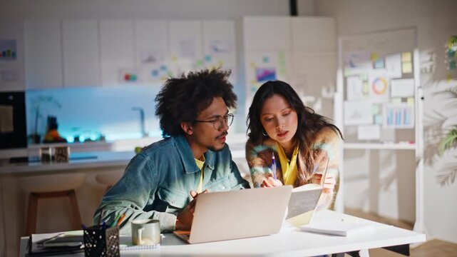 Multiethnic coworkers discussing ideas laptop. Night home office brainstorming.