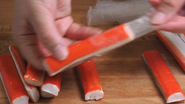 Cook removes the packaging from the crab sticks on a wooden table. Fish delicacies for preparing the dish. Close-up
