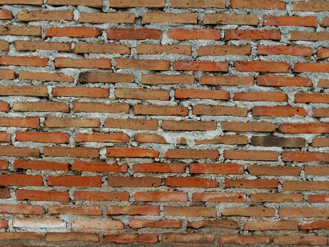 Texture of an unfinished red brick wall with messy and uneven grey cement mortar during construction