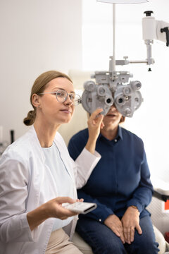 Optometrist adjusting phoropter device, performing eyesight examination for senior woman during visit in ophthalmology clinic. Vision checkup, glasses prescription, eye diagnostics, modern optometry