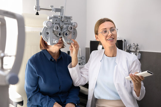 Woman looks in phoropter during eye sight testing, female optometrist conducts professional vision checkup, eyesight assessment using modern medical equipment at patient visit in ophthalmology clinic