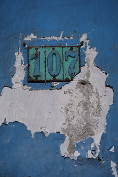 Vintage metal house number plaque 107 on damaged blue painted wall. Photographed in Surabaya, Indonesia on September 9, 2026.