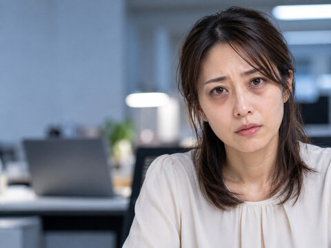 オフィスで目の下にクマがある疲れた表情の女性　残業と睡眠不足のイメージ