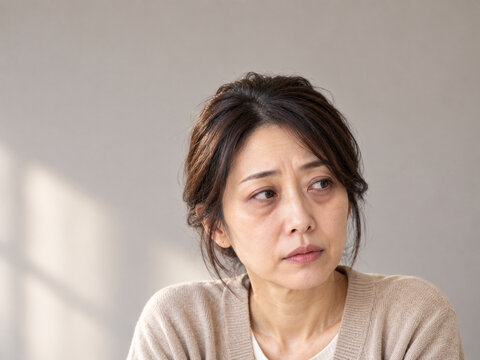 目の下にクマとたるみが目立つ横目の中年女性　窓辺の光でみる年齢肌の悩み