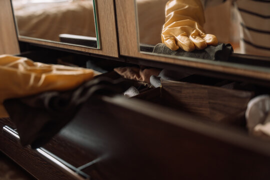 Gloved hand and reflection wiping a ledge above an open drawer with a dark cloth.