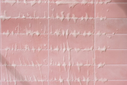 White cleaning foam dripping along horizontal pink tile rows in close view.