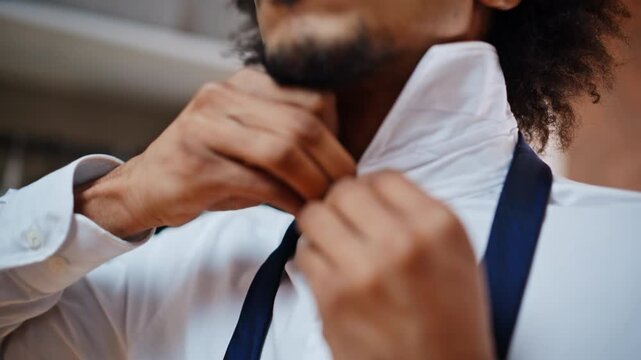 Tying necktie close up. African american man knotting blue tie white shirt home