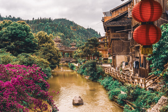 Wooden stilt houses beside a river with red lanterns and blooming flowers, Xijiang, Guizhou, China