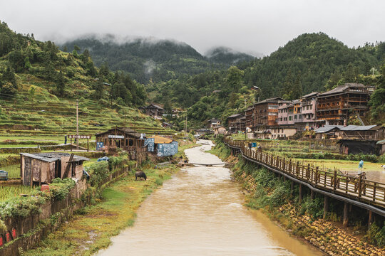 Village road beside a river and wooden houses in misty mountains, Xijiang, Guizhou, China