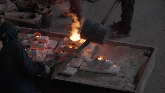 Workers move a hot ladle above a row of ceramic shells and tilt it again to pour molten metal into the next mold.