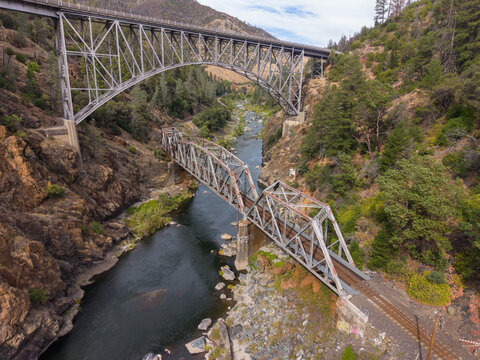 Two impressive bridges, an arched vehicle bridge and a railroad truss bridge, spanning the deep Feather River canyon with lush green and dry vegetation