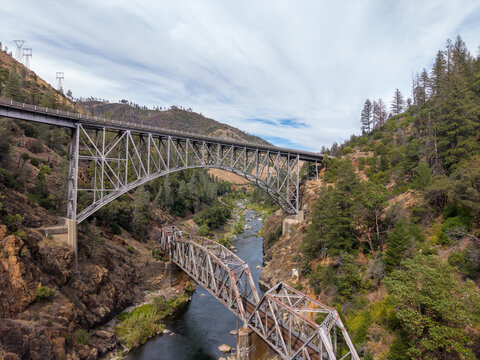 Two distinct steel bridges, one modern arch and one old truss, traversing the rugged Feather River canyon, showcasing engineering across different eras in the California landscape