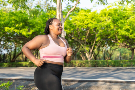 African Black plus-size woman jogging along pathway in the garden. 