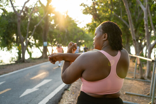 Rear view of plus-size woman stretching body and exercise outdoors in garden. 
