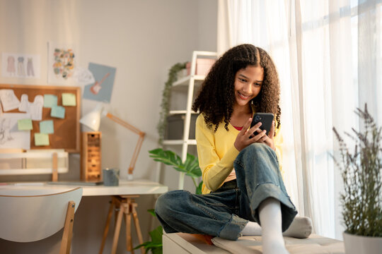 African American teenage girl using cellphone while sitting on cabinet