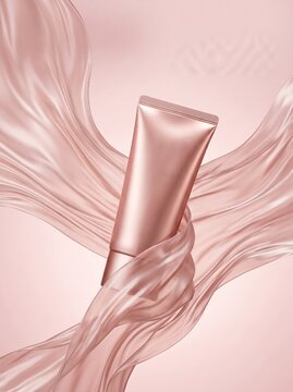 A rose gold cosmetic tube elegantly wrapped in flowing pink silk fabric, against a soft pink background.