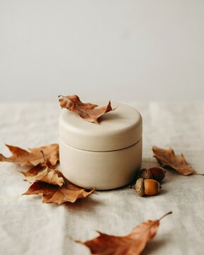 Minimal Autumn Skincare Jar with Dried Leaves and Acorn on Neutral Background
