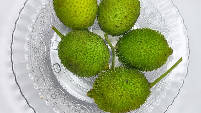 Fresh spiny bitter gourd fruits arranged on circular glass plate overhead view.