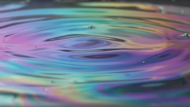 Abstract close up of iridescent oil slick ripples on water surface.