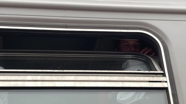 The teenage girl is lying on the upper bunk of the train compartment and thoughtfully gazing into the distance through the open window. A journey, a train trip. A view from the platform.