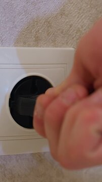 Close up view of empty power socket. hand plugs and unplugs black electrical plug into white circular port on textured wall outlet plugging unplugging