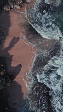 Aerial pastel sand gentle waves lapping quiet shore, soft foamy edge meeting warm beige beach, long coastal shadows and subtle film grain, meditative minimalist atmosphere, vertical video