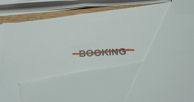 Close-up of a person crossing out the word Booking on paper. Concept for canceled reservation, changed plans, travel cancellation and appointment removal.