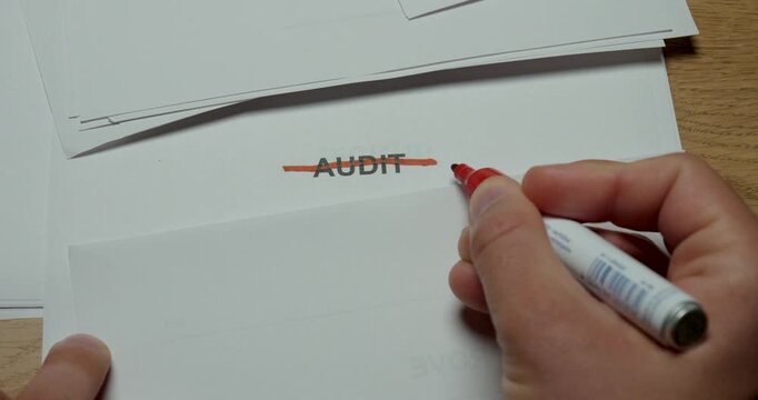 Close-up of a person crossing out the word Audit on paper. Concept for canceled inspection, completed review, compliance process and business assessment.