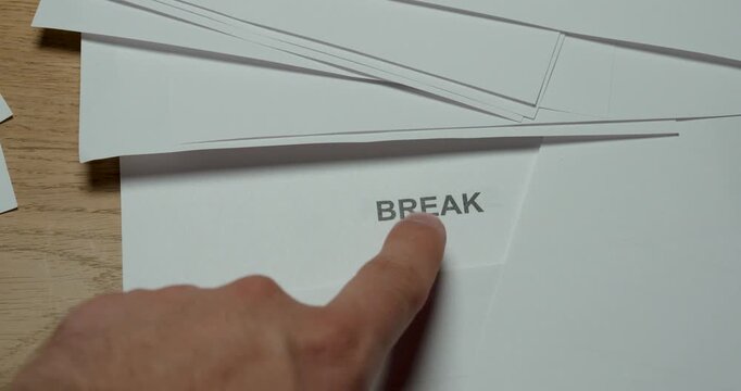Close-up of a hand removing a sheet of paper to reveal the word Break and pointing at it with a finger. Concept for taking a break, rest, pause, work-life balance and time management.