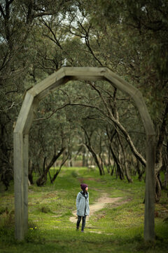 A woman walks beneath a wooden arch and along a winding path through a tranquil woodland, Donald, Victoria, Australia