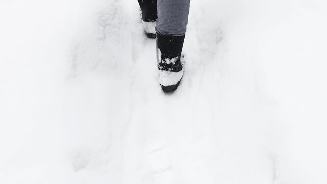 Person walking through a snow-covered path in winter, with boots partly buried in fresh powder. Cold weather, outdoor travel and seasonal nature concept.