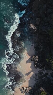 Aerial hidden cove turquoise surf curling into small sandy bay, dramatic dusk light over rocky cliffs and emerald water, secluded mood with foaming inlet and cinematic texture, Vertical video