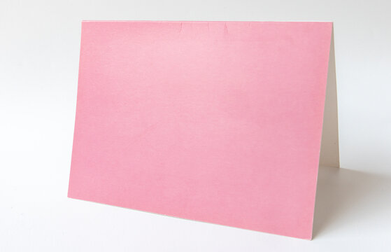 Blank folded pink paper greeting card or invitation card casting a soft shadow, isolated on a white background. Empty standing half-open pink table tent card mockup template with copy space. 