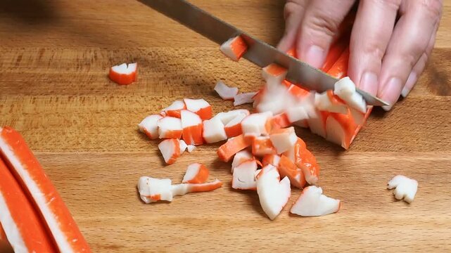 The cook cuts crab sticks on a cutting board into slices. closeup.